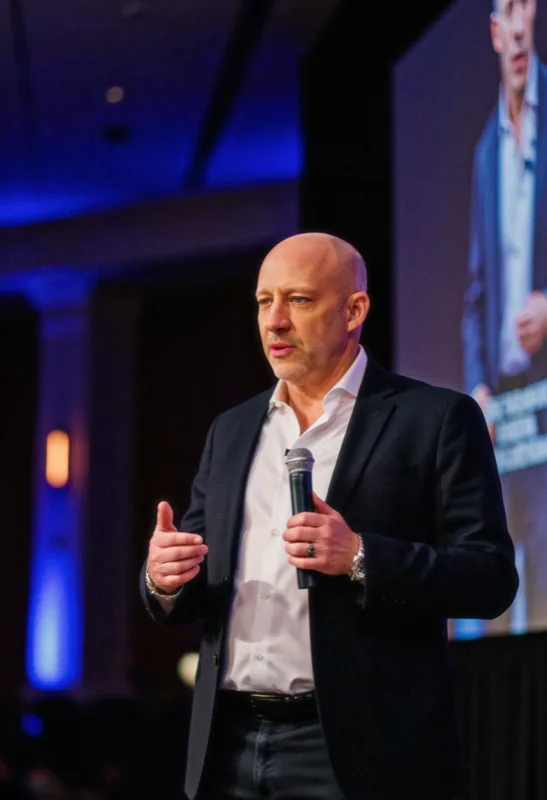 Chris Daigle on stage mid-talk, holding a microphone